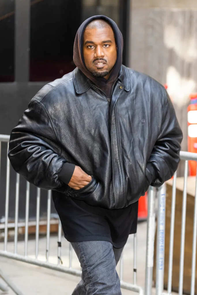 Kanye West wearing a black leather jacket and a dark hoodie with his hands in his pockets.