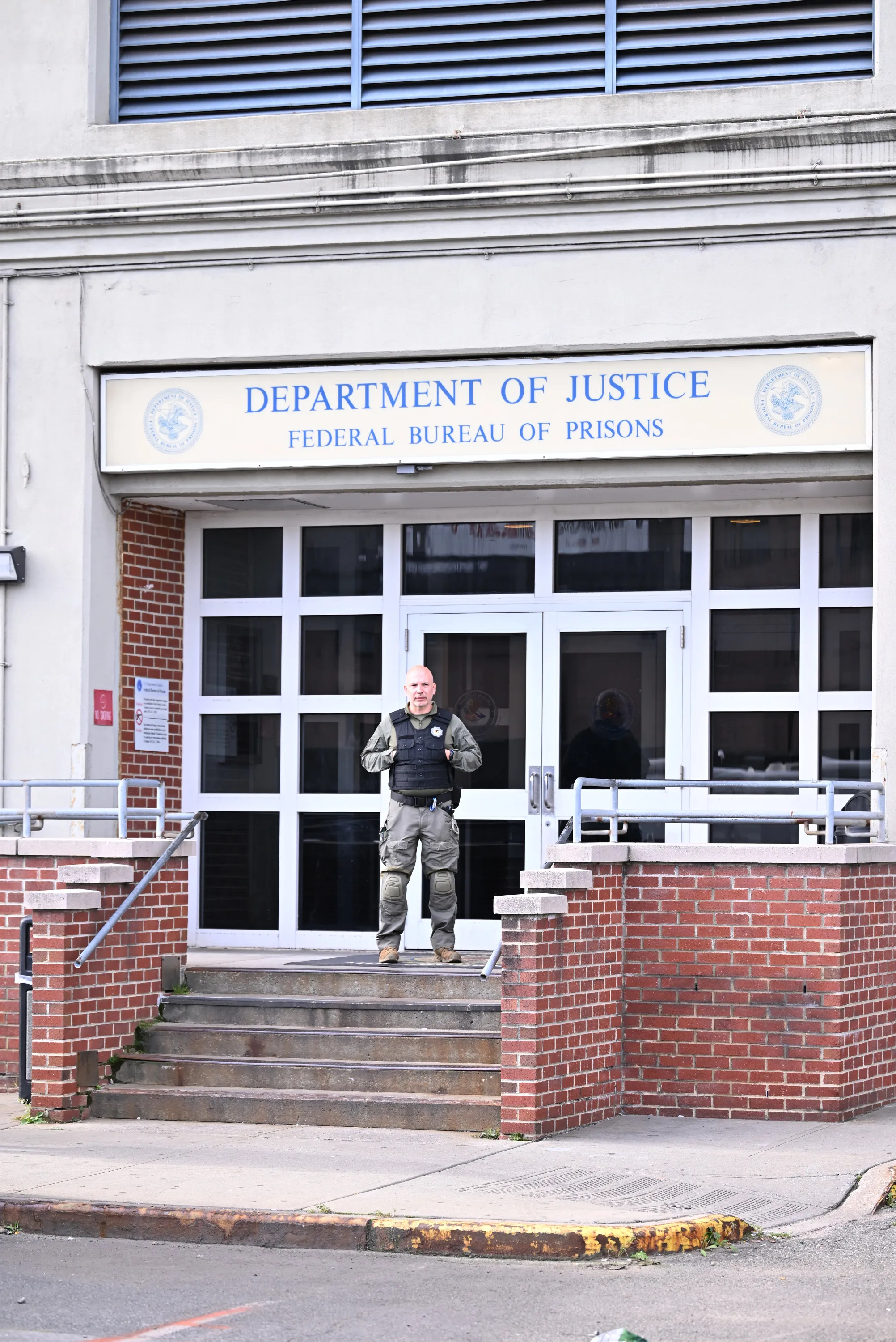 An armed law enforcement officer stands guard outside the entrance of the Metropolitan Detention Center in Brooklyn.