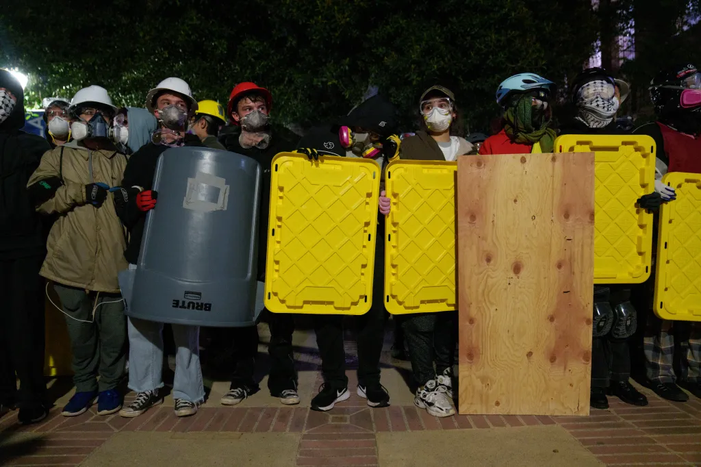 Pro-Palestine protestors stand with shields across from members of law enforcement in an encampment at UCLA.