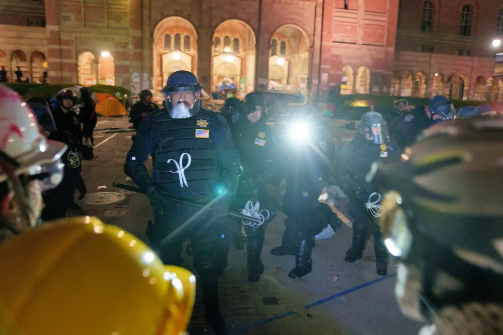 Law enforcement officers in riot gear stand outside a campus building during a protest.