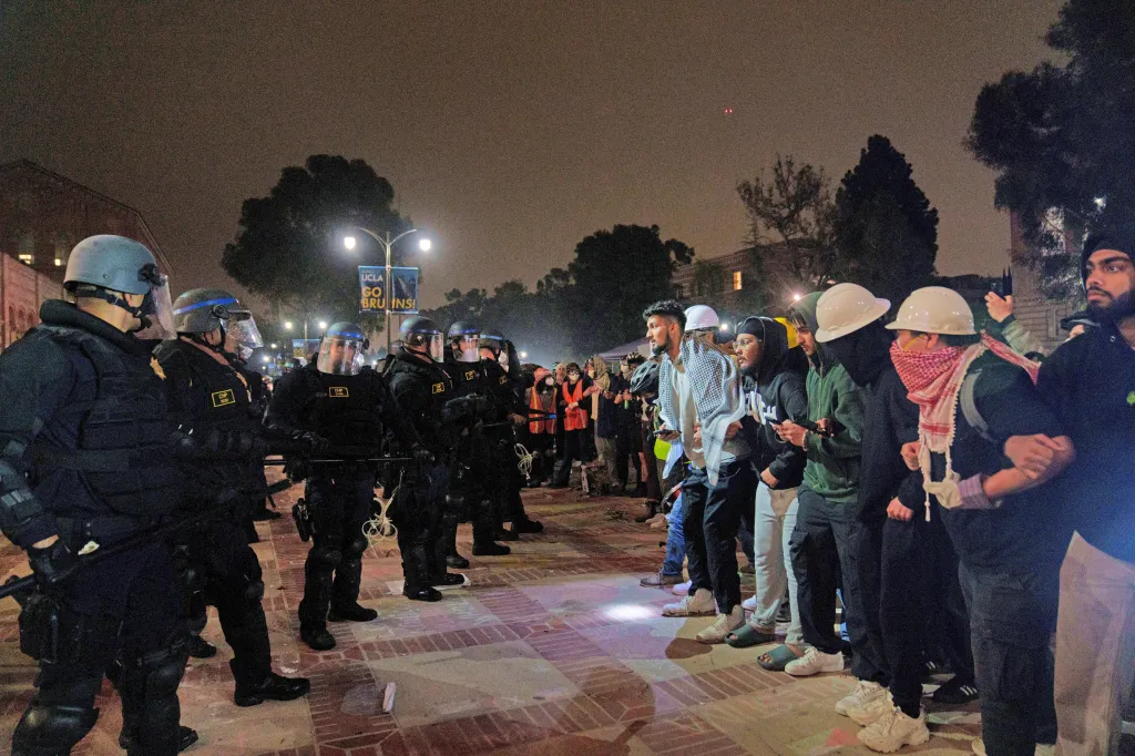 Law enforcement officers in riot gear confront a line of students and protesters at UCLA.