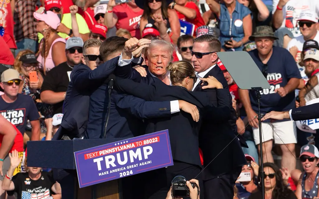 Donald Trump is escorted off the stage by Secret Service agents, with blood visible on his face, following an incident at a campaign rally.