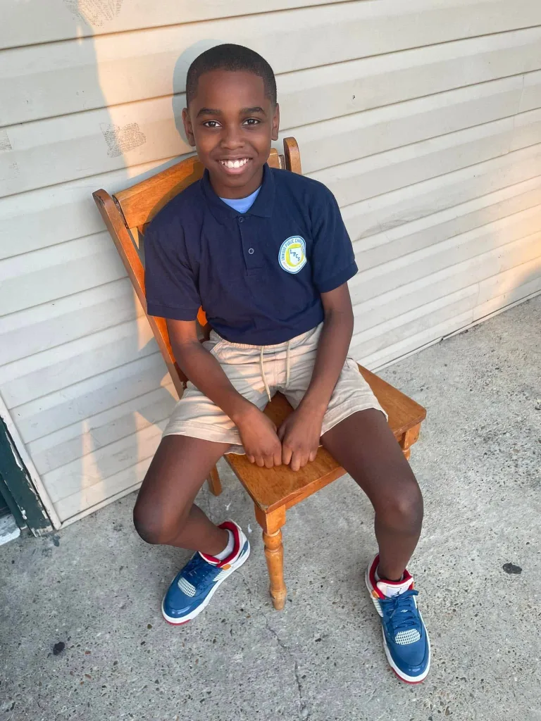 Photo of Sha'Michael Russell smiling while sitting on a wooden chair.