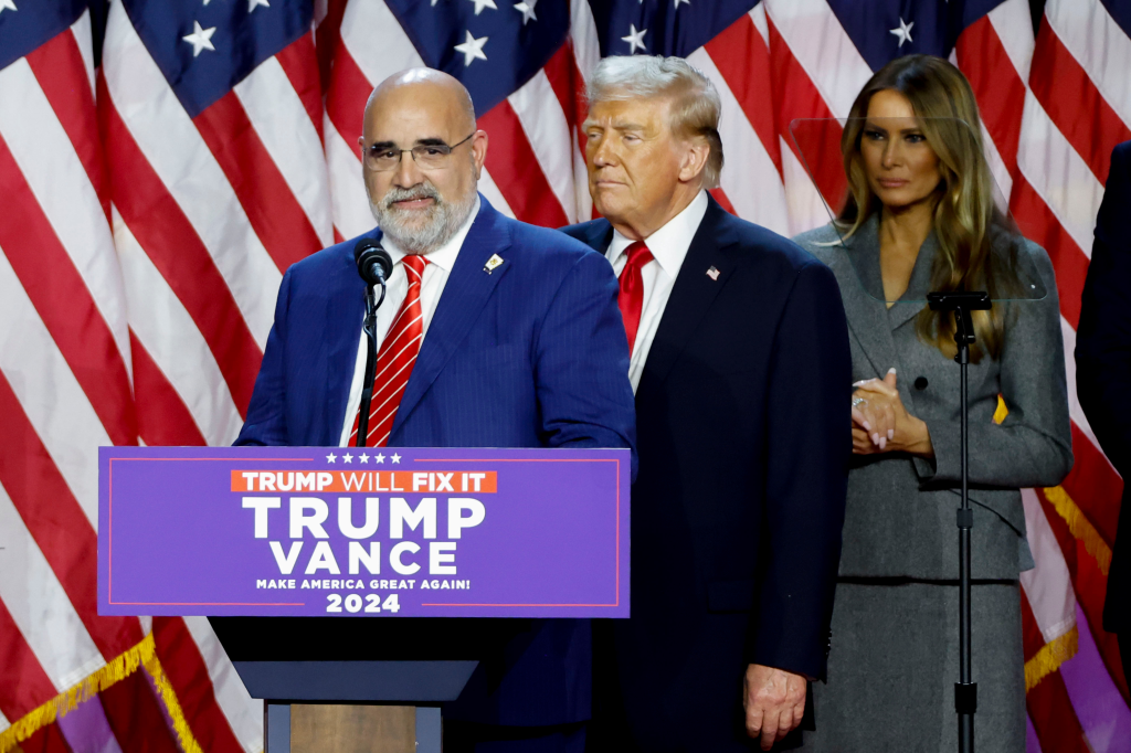 Chris LaCivita, Donald Trump, and Melania Trump stand before American flags at an election night event.