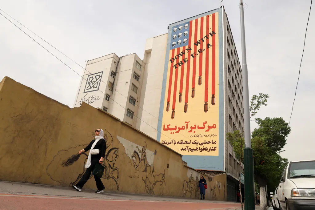 Women walk past a building in Tehran featuring a large anti-U.S. mural with skulls on the flag and the slogan 