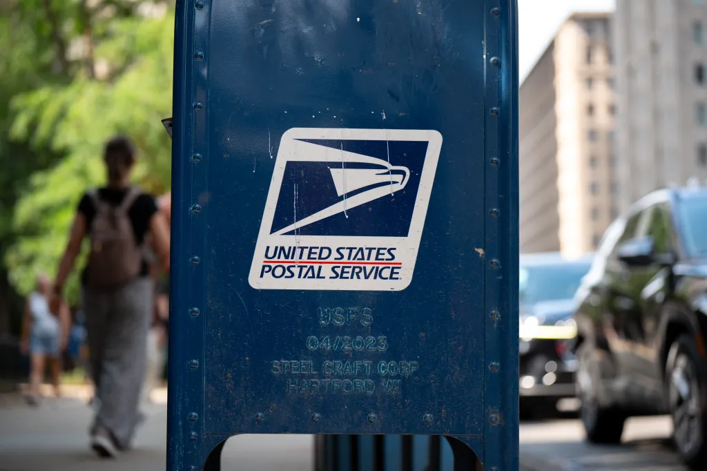 A close-up of a blue United States Postal Service mail collection box on a city street.