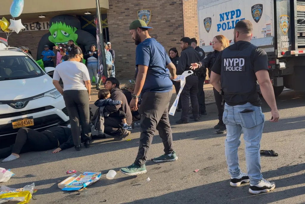 Emergency personnel and bystanders gather at the scene of a vehicle crash outside the NYPD 83rd Precinct.