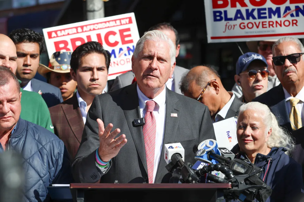 Bruce Blakeman, candidate for New York State Governor, speaks at a podium surrounded by supporters and local politicians in Queens.