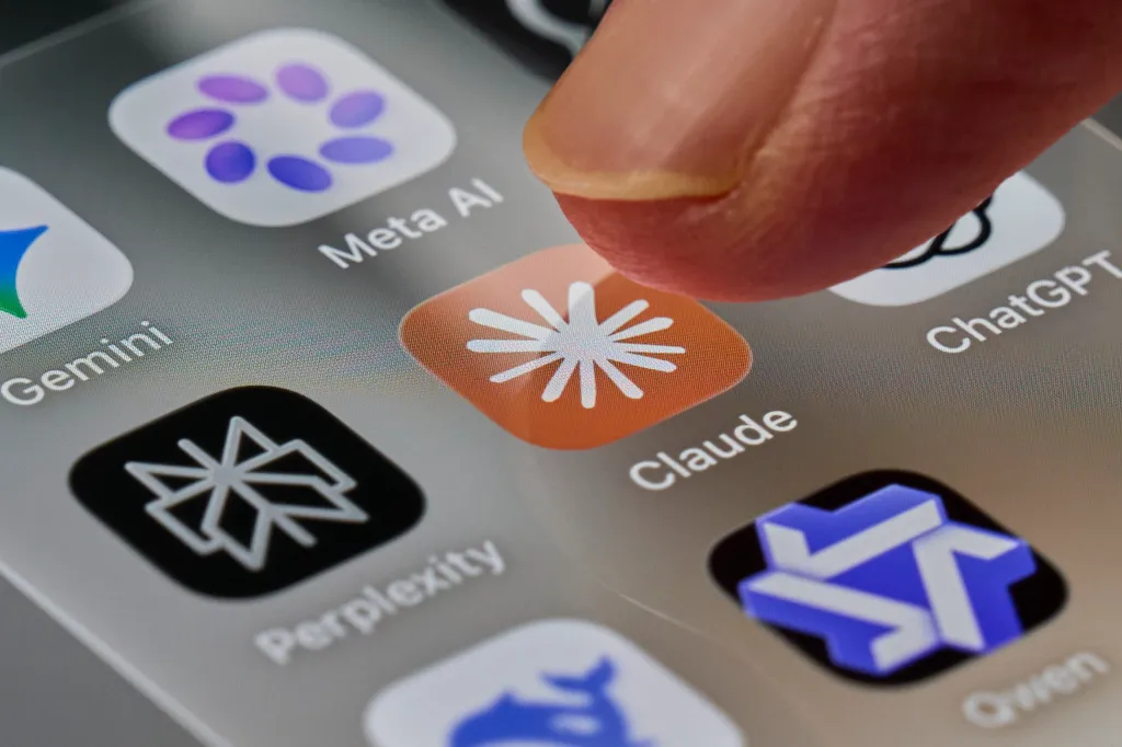A finger tapping the Claude app icon on a smartphone screen surrounded by other AI chatbot apps.