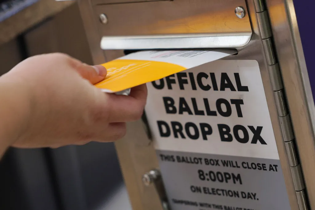A person casts their ballot into an official ballot drop box.