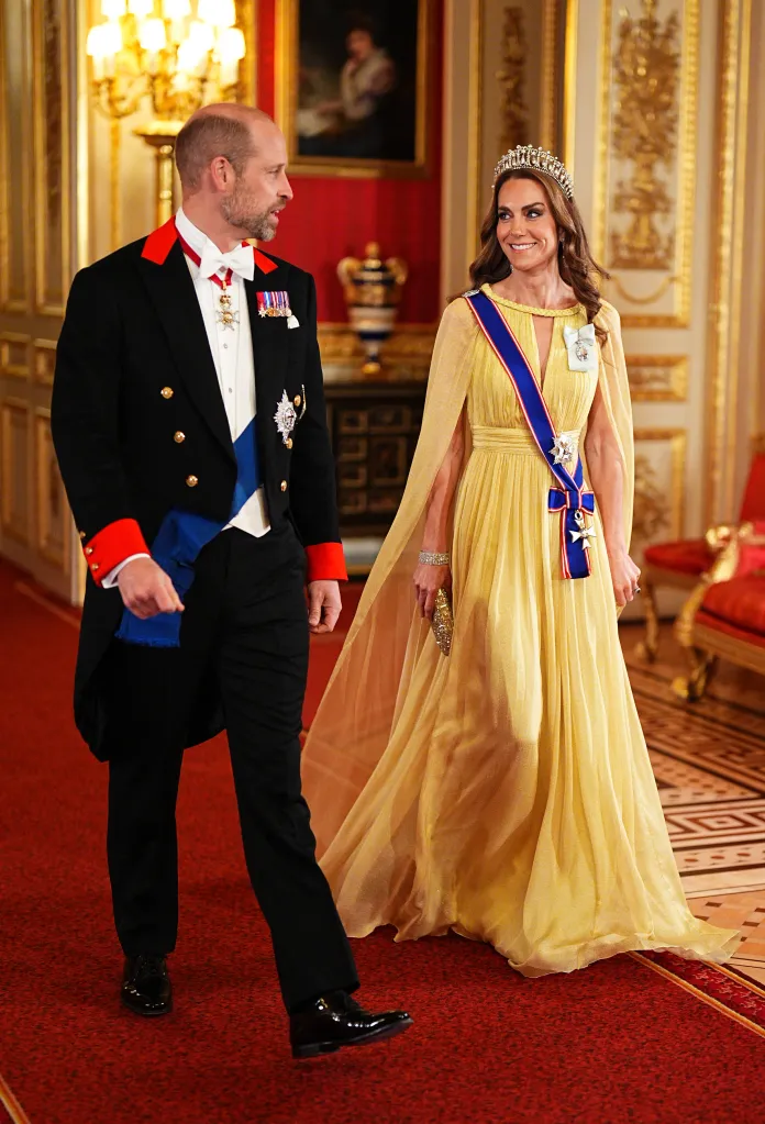 Prince William, in coat and tails and a blue sash and medals, and Catherine, Princess of Wales, in a golden gown with blue sash and medals, arrive for a State Banquet at Windsor Castle.