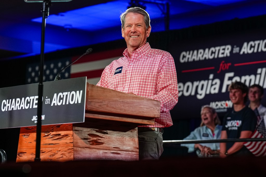 Georgia Governor Brian Kemp speaks at a campaign event behind a podium with a sign that reads 