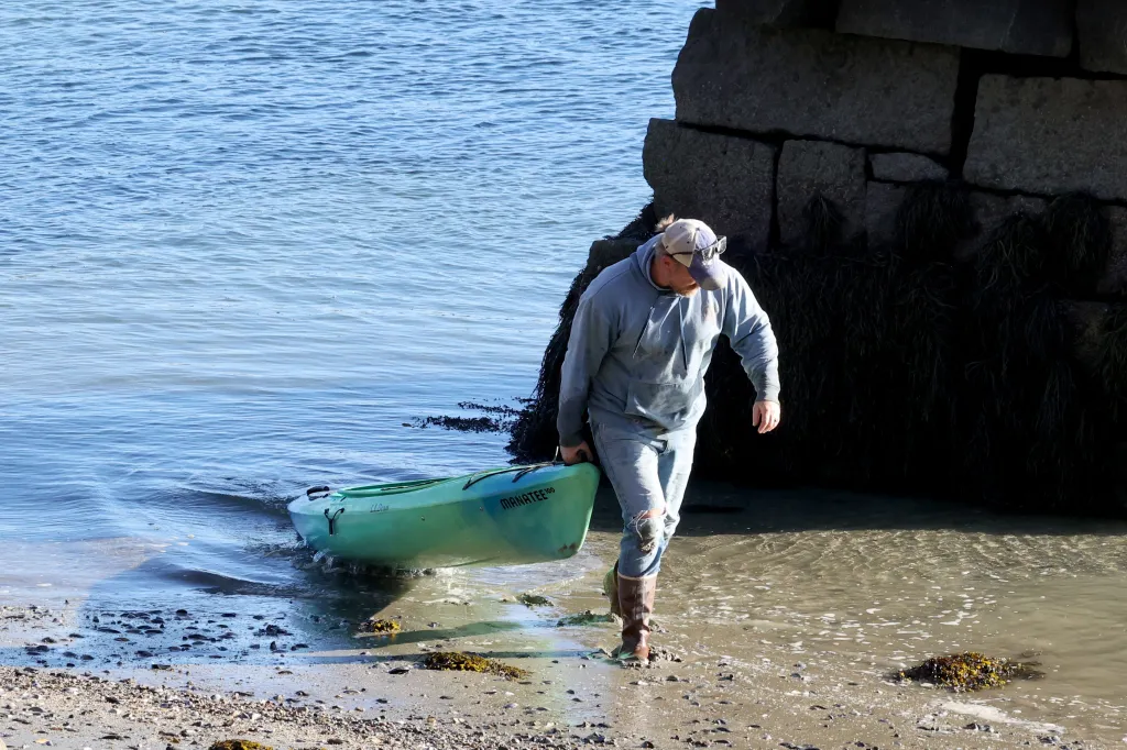 Graham Platner walks ashore carrying a green canoe in Sullivan, Maine.