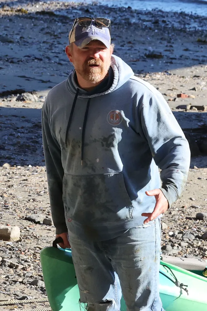 Graham Platner stands on a shore in Sullivan, Maine, holding a green canoe.