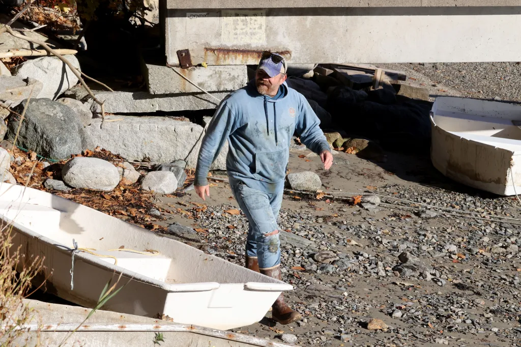 Graham Platner walks along a rocky shore near boats.
