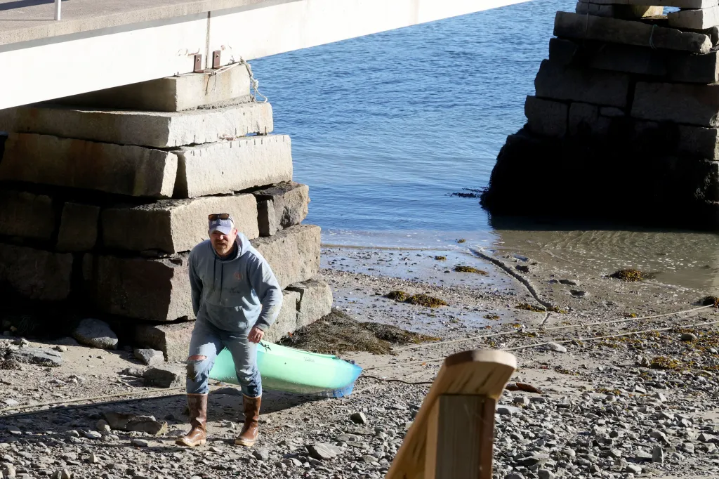 Graham Platner pulls a canoe onto the shore beneath a bridge after a day of oyster fishing in Sullivan, Maine.