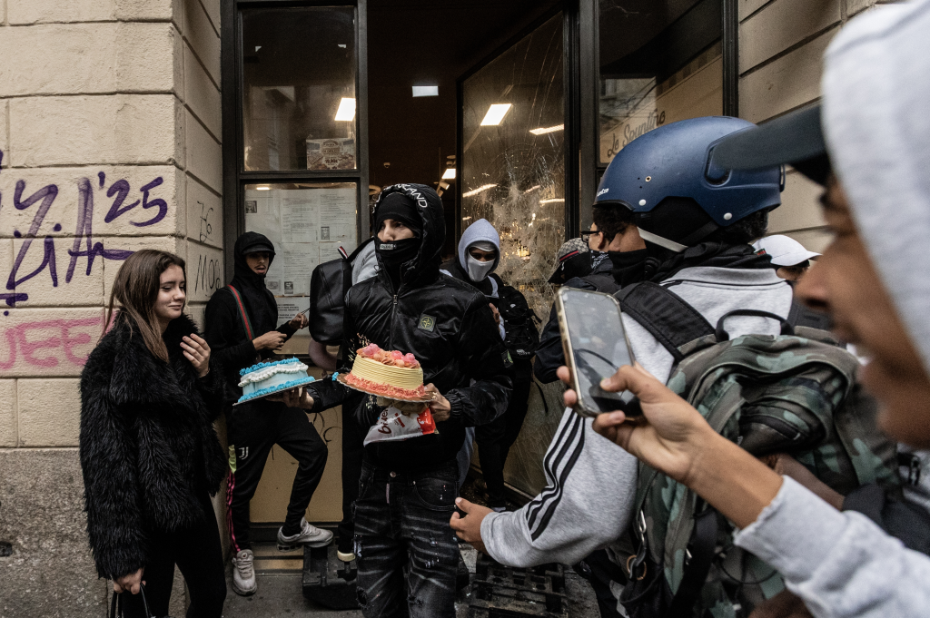 Protesters holding looted cakes in front of a vandalized shop during unrest in Milan.