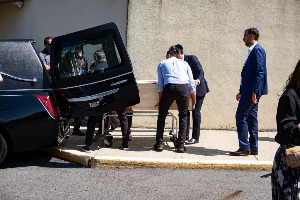 Matthew Rahmani stands near a hearse as a casket is loaded following the funeral of his wife, Allison Rahmani.