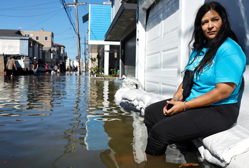 Alexandra Cifuentes sits on sandbags in front of her home as high tide coastal flooding impacts Sunset Beach in Huntington Beach.