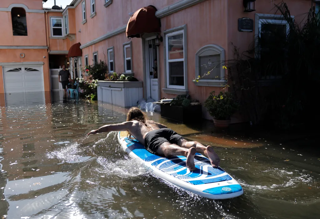 Morgan Wynne paddles on a surfboard through coastal floodwaters outside his home.
