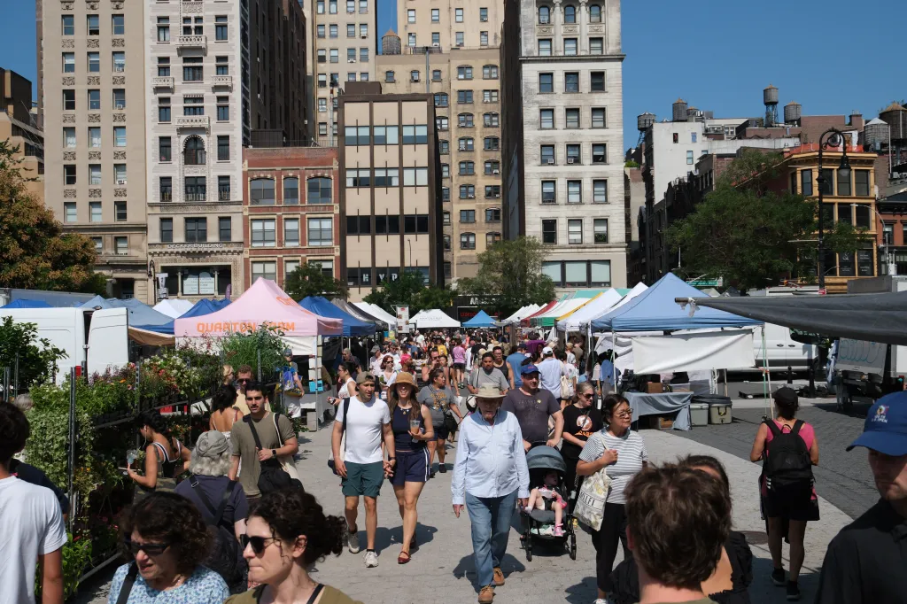 A crowded street market with numerous tents set up against a backdrop of tall city buildings.