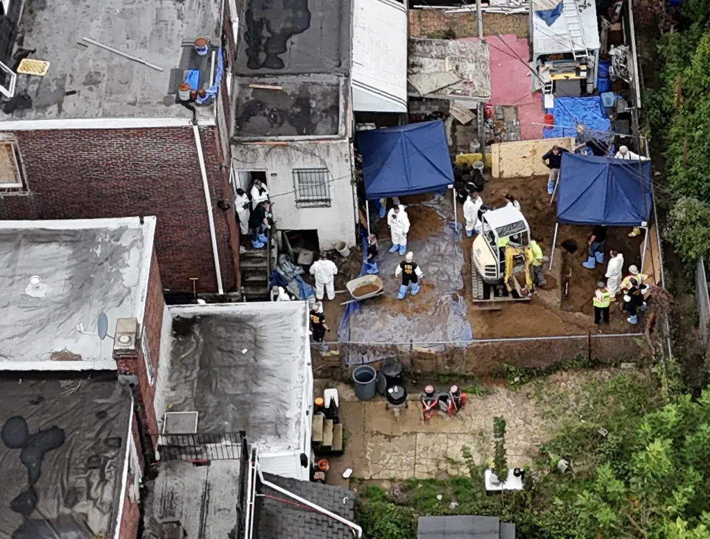 FBI Evidence Response Team agents excavate the backyard of Eugene Horsch's home using a small digger and manual tools under two blue pop-up tents.