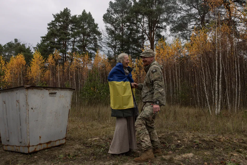 Ukrainian serviceman Dmytro holds hands with his partner Larysa, wrapped in a Ukrainian flag, after her evacuation from Oleshky.