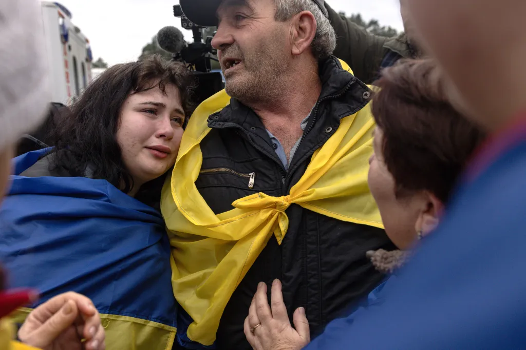 Family members embrace as a man wrapped in a Ukrainian flag arrives after evacuating from Oleshky.
