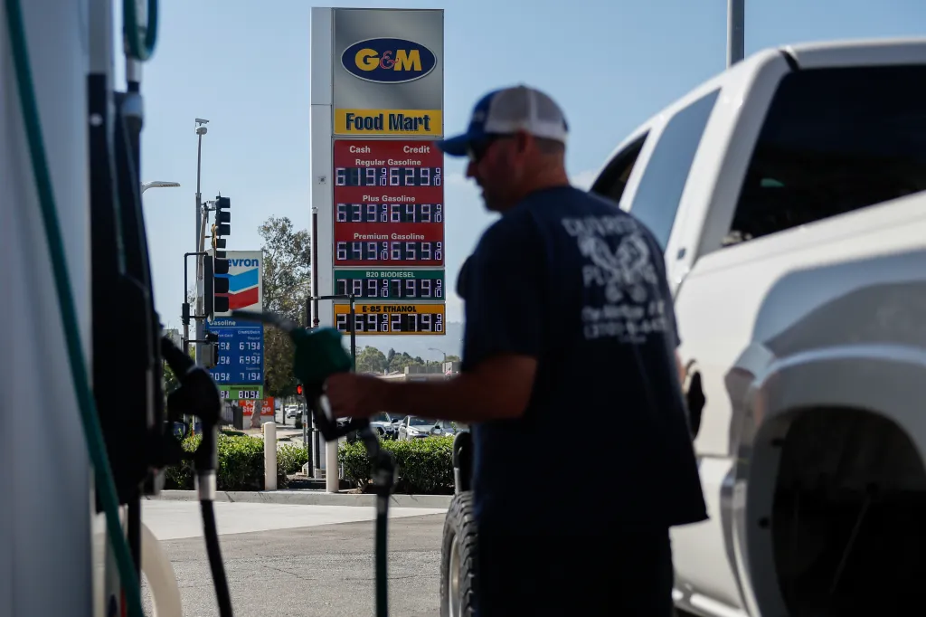 A driver refuels a vehicle with diesel fuel at a G&M gas station in Torrance, California, with a sign displaying fuel prices in the background.