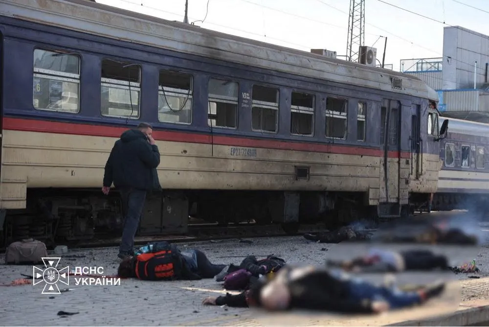 A man walks past bodies lying on the ground next to a damaged train carriage at a railway station following a drone strike.