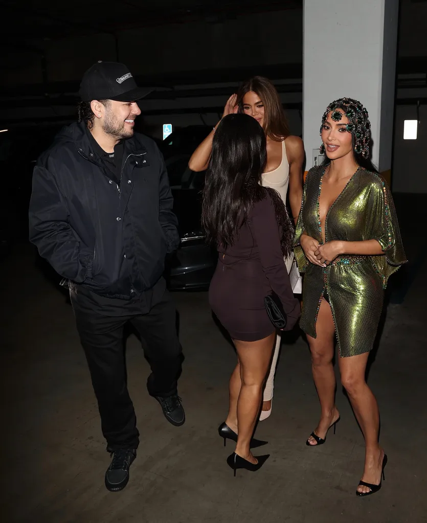 Kim Kardashian, wearing a green sequin dress and jeweled headpiece, stands with Rob Kardashian, Kourtney Kardashian, and Khloé Kardashian in a parking garage.