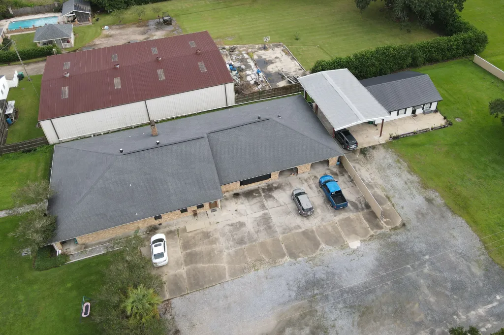 An aerial view of Ken Urker's family residence in Raceland, Louisiana, showing multiple buildings, vehicles parked on the driveway, and surrounding green property.
