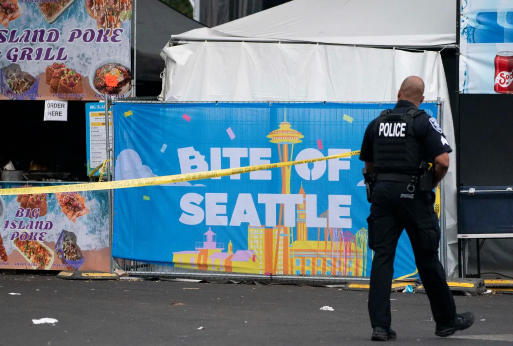 A police officer walks by a sign for the Bite of Seattle food festival after three people were killed in a shooting on July 26, 2026.