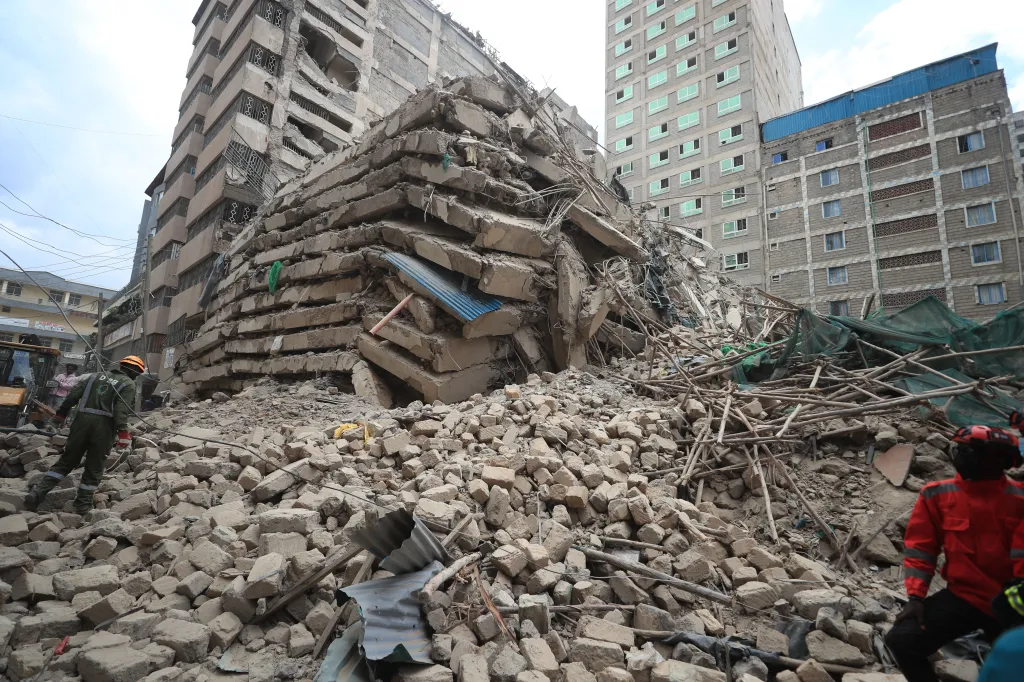 The site of a collapsed 18-story building in Nairobi, Kenya, showing stacked concrete slabs and rubble, with rescue workers nearby.