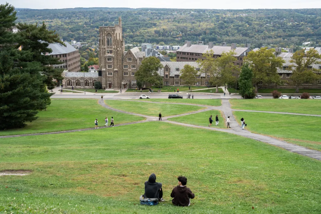 Students relaxing on Libe Slope at Cornell University, with campus buildings in the background.