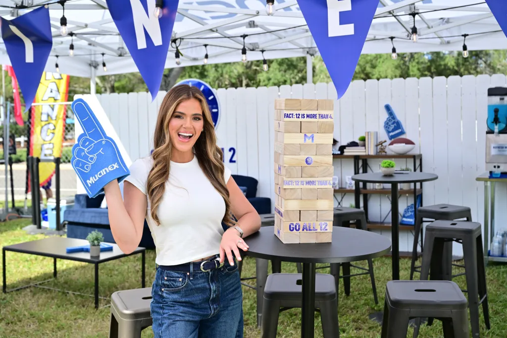 JoJo Fletcher smiles while holding a Mucinex foam finger at a tailgate.