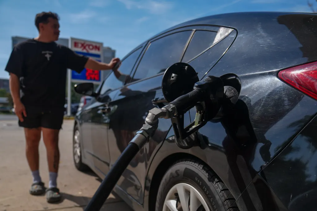 A man fuels a black car at an Exxon gas station.