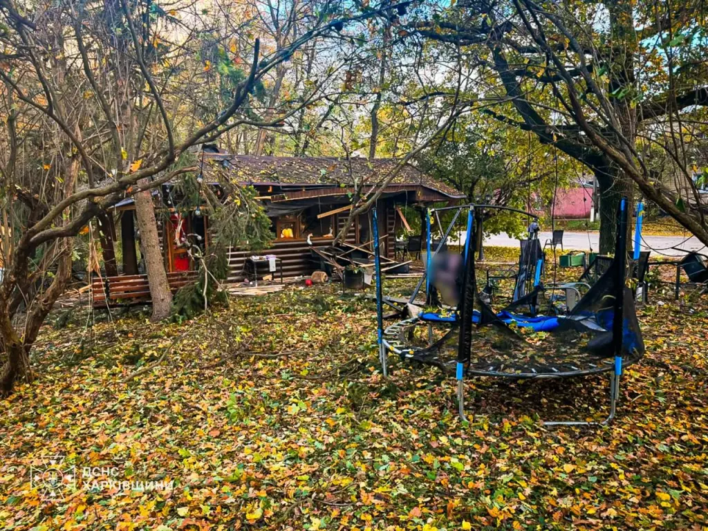 Aftermath of a drone strike on a park in the Kharkiv region, showing damaged buildings and debris among fallen autumn leaves.