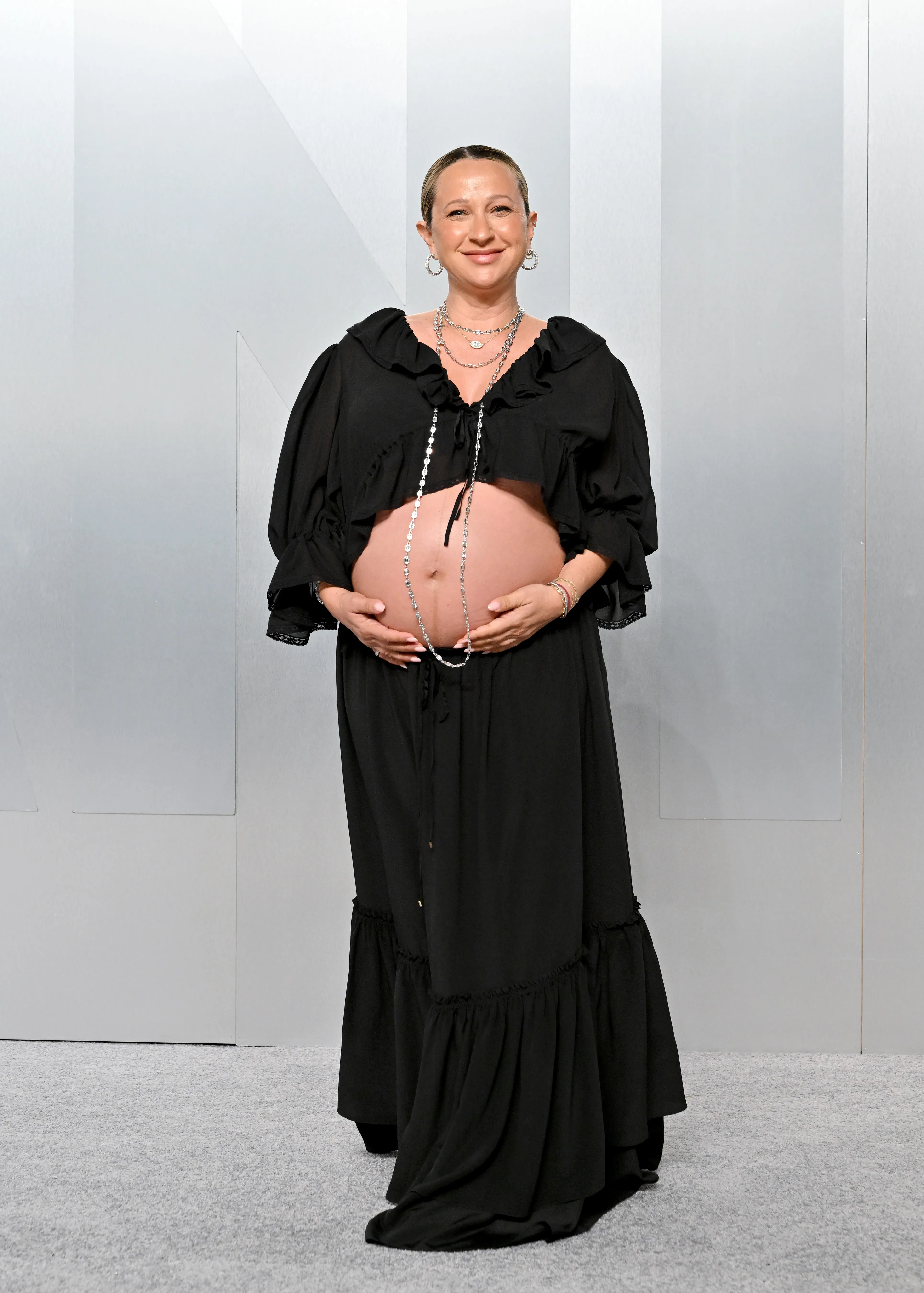 Jennifer Meyer attends the Vanity Fair Oscar Party wearing a black two-piece outfit with her hands resting on her baby bump.