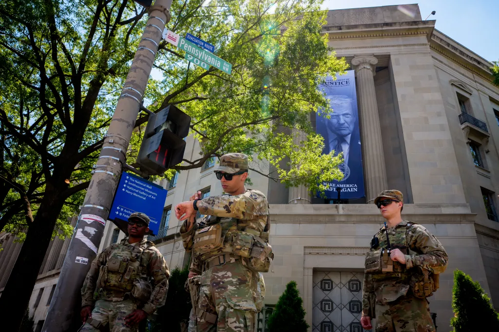 National Guard members stand outside the Department of Justice building beneath a banner of U.S. President Donald Trump.