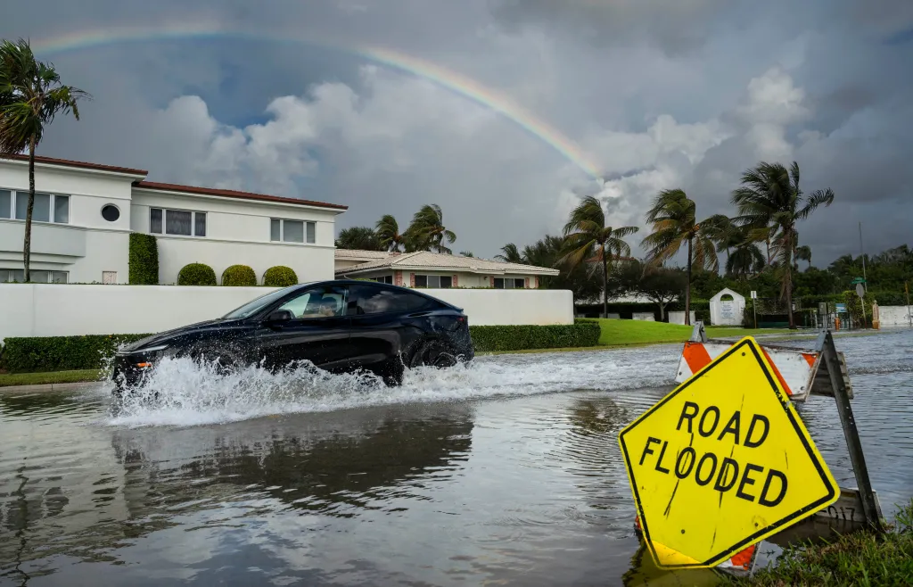A motorist drives a car through floodwaters on Flagler Drive past a 