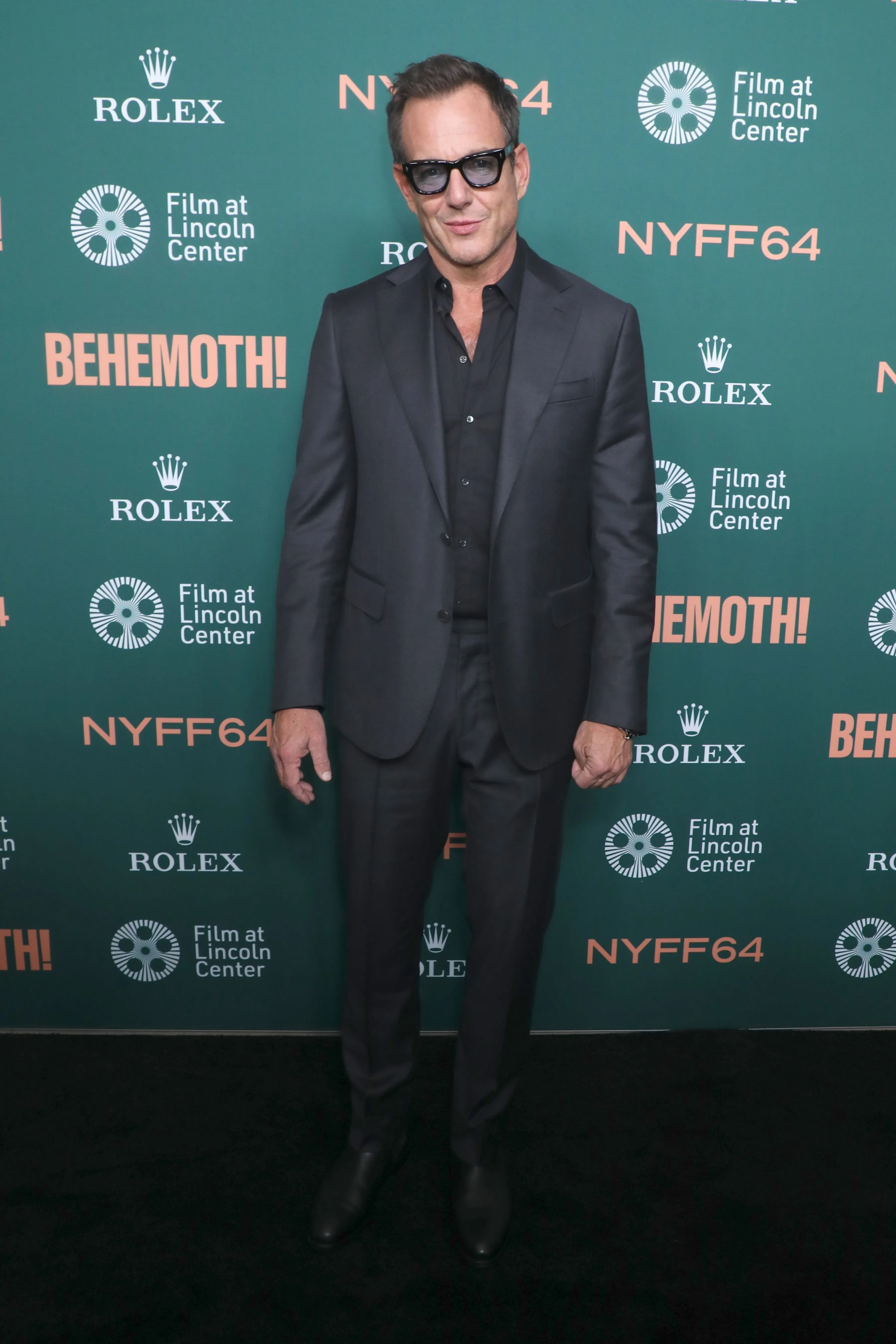 Will Arnett standing in a dark suit and sunglasses on the green carpet at the 'Behemoth!' premiere.