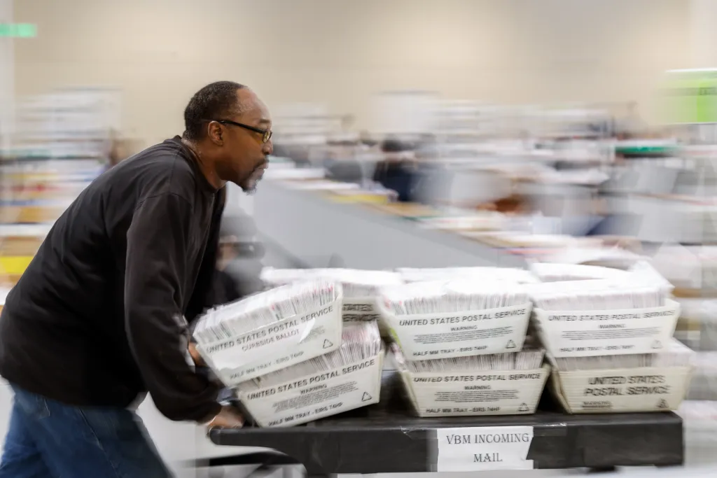 A worker pushes a cart loaded with USPS bins containing mail-in ballots during the election count.