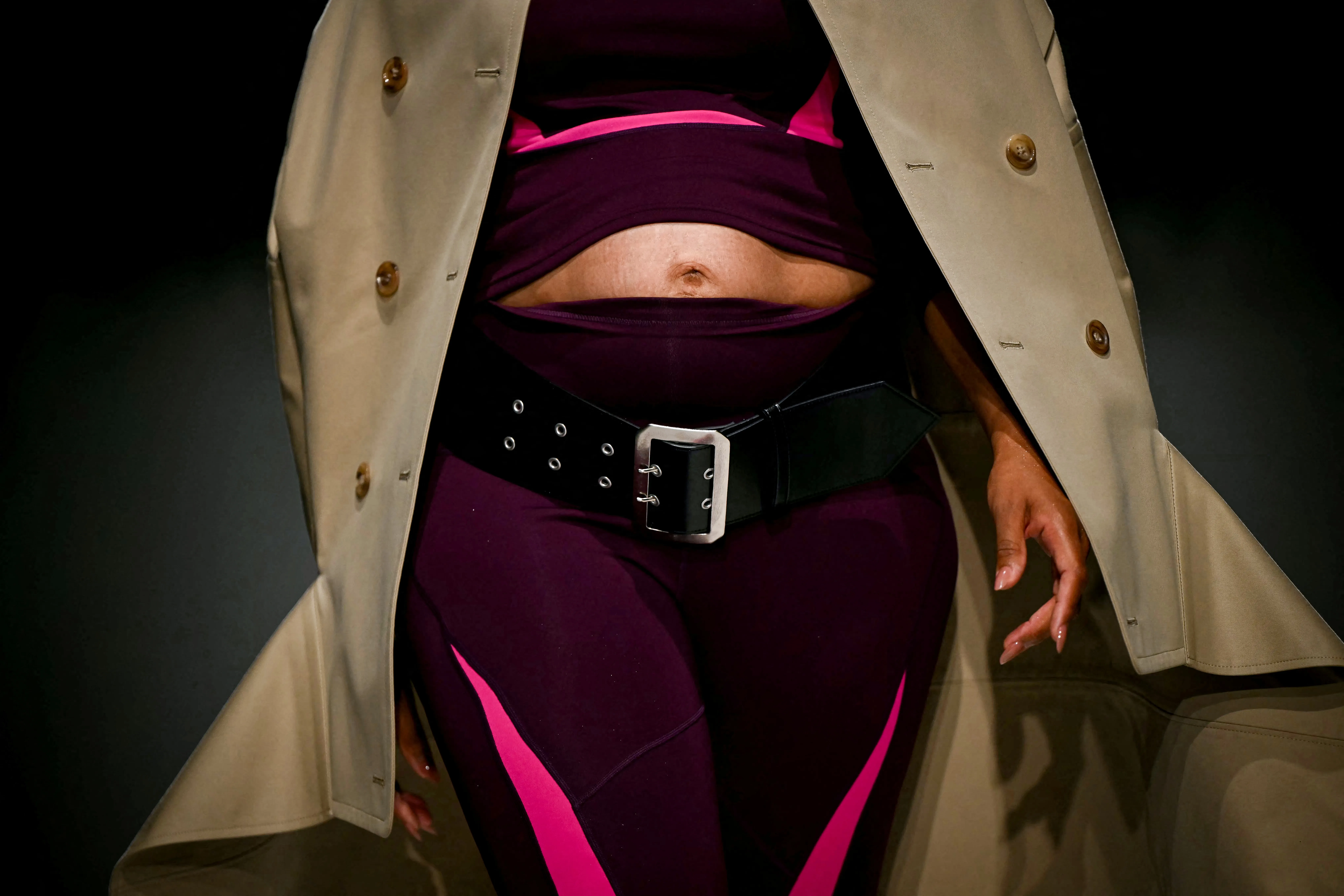 US singer Ciara models a creation for the Junya Watanabe Women's Spring/Summer collection fashion show in Paris, wearing a beige trench coat over a plum-colored athletic outfit featuring pink accents and a thick black belt.