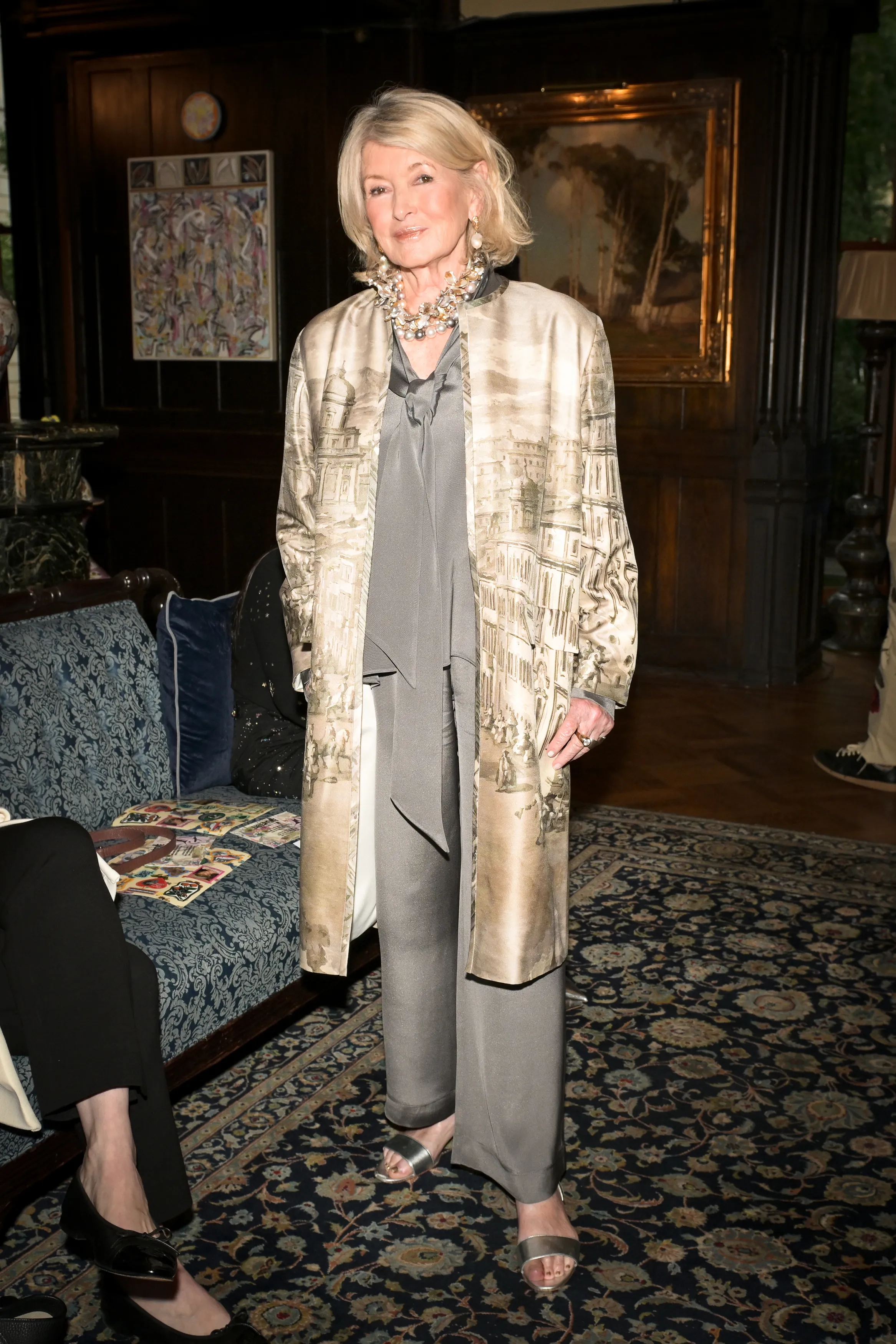 Martha Stewart wearing a grey silk pant suit, a matching tie blouse, and a patterned coat during the Libertine fashion show.