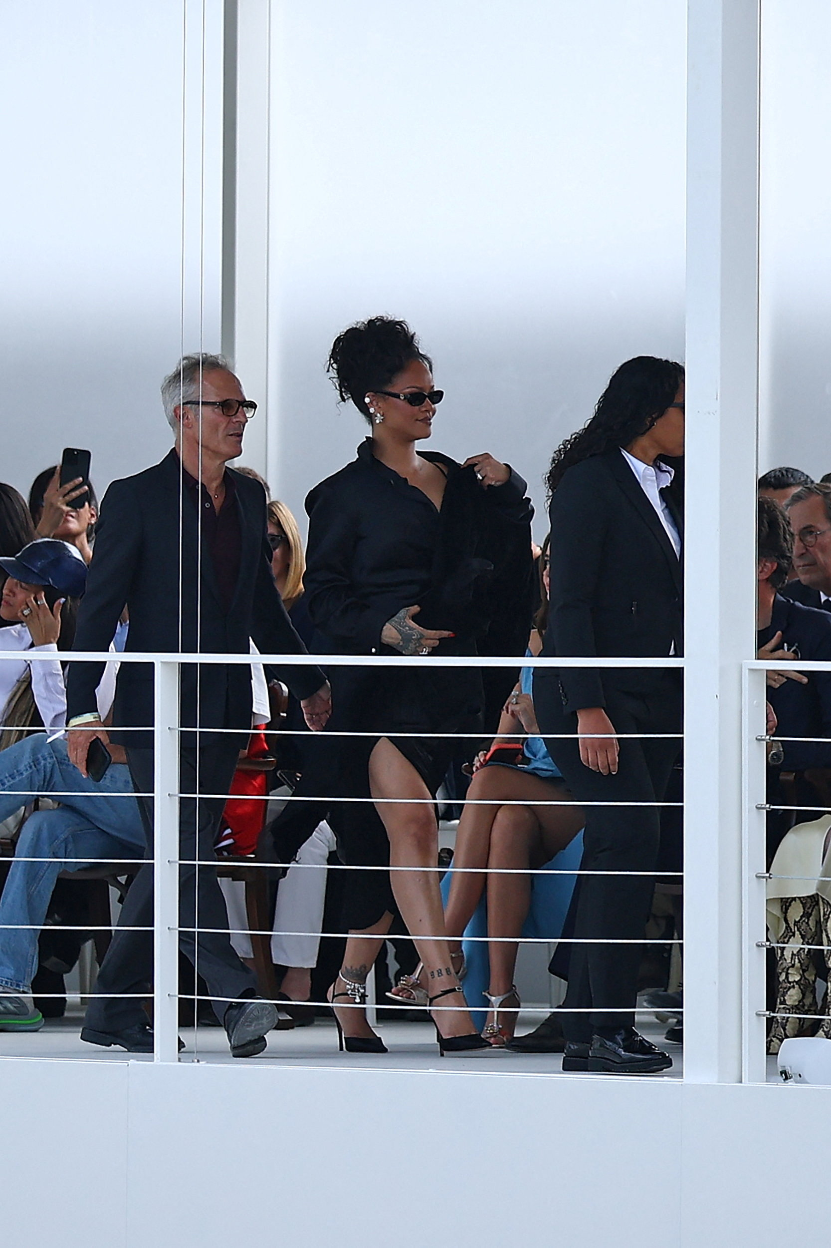 Rihanna arrives at the Dior Spring/Summer collection show, flanked by companions and security personnel.