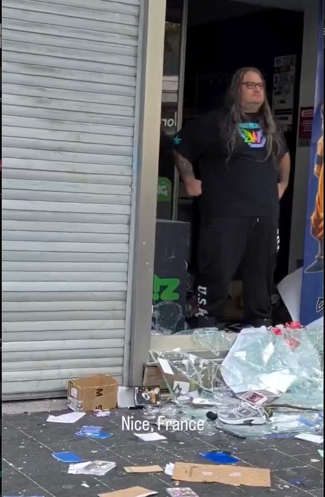 Pierre, a sales assistant, stands in the shattered doorway of a video game store in Nice, France, after rioters attempted to loot the shop.