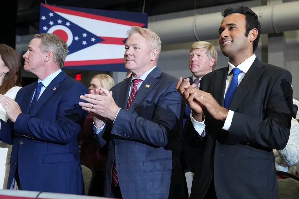 Republican politicians in suits applaud in front of an Ohio state flag.