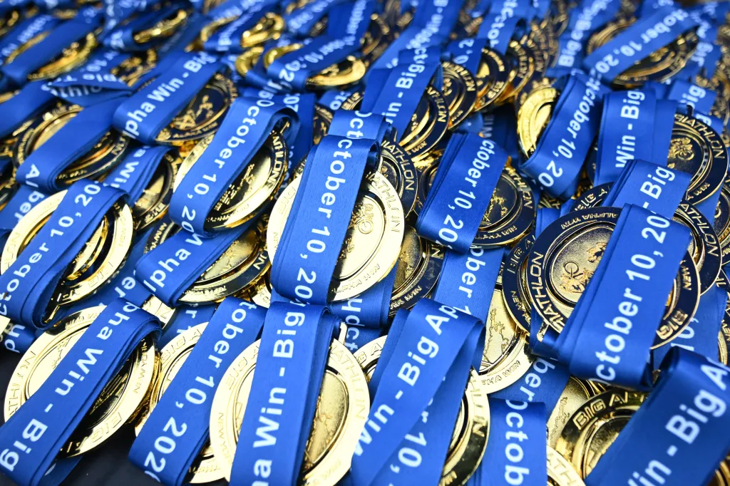 A pile of gold finisher medals with blue ribbons from the Big Apple Triathlon.