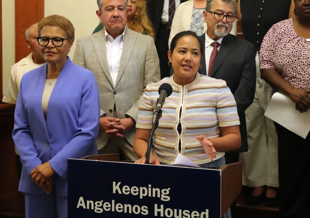 Council member Ysabel Jurado speaks at a podium with Mayor Karen Bass standing to her left during a press conference about affordable housing funding in Los Angeles.